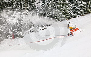 Snow gun spraying artificial ice crystals over ski piste, snowmaking in winter sports resort, trees in background