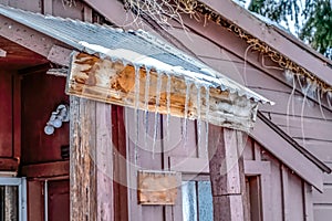 Snow and icicles on the corrugated metal roof of an old cabin in winter season