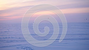 Snow kiteboarders in a snowy field against the backdrop of a sunset