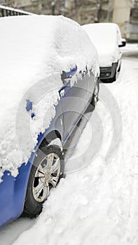 Snow layer on windscreen, window of sedan in city street driveway parking lot spot. car stuck after heavy blizzard