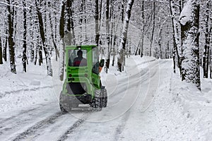 snow machine, green tractor cleans the snow from the snow in the background of the forest. back view