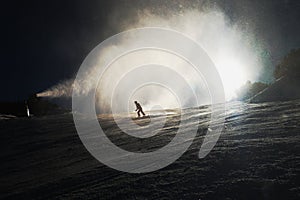 Snow making on slope. Skier near a snow cannon making fresh powder snow. Mountain ski resort in winter calm.