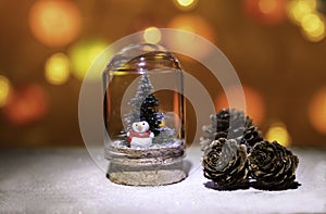 Snow man with Christmas tree in glass tube near pine cone from Christmas light background