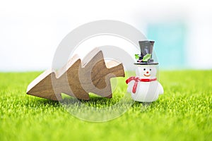 Snow man doll with top hat and wooden Christmas tree on green fiel with space on blurred background