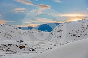 Snow mobile with metal trailer parked on the rocky side of a small snow covered mountain in the Arctic