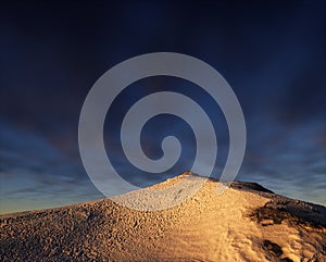 Snow mountain at sunset under a blue sky with clouds.