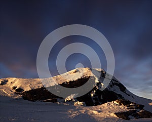 Snow mountain at sunset under a blue sky with clouds.