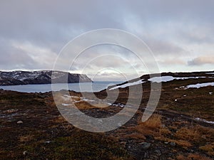 Snow patches on mountain landscape with blue sea and fjord in the background, northern norway