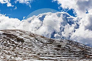 Snow patches on mountains and fluffy clouds on bright sunny day