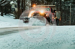Snow plow at dusk maintains roads in a residential neighborhood during snow storm