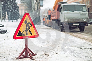 Snow-plow remove snow from the city street.Warning road sign.Winter service vehicle snow blower work.Cleaning snowy