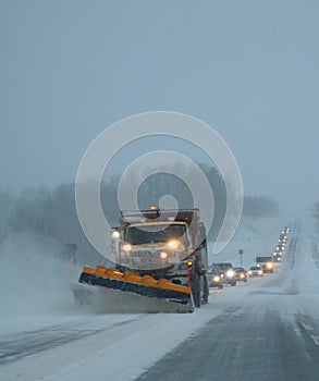 Snow plow scraping snow off a busy Ontario road with trail of cars behind