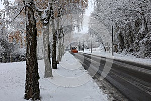 Snow plow is sprincling salt or de-icing chemicals on pavement in city