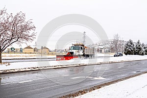 Snow plow truck on a wet paved road with snowy sidewalks on a cloudy winter day