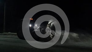 snow removal equipment in the form of a tractor operating at night and throwing snow off the roadway into a ditch