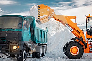 Snow removal after snowfall and blizzards. Excavator loads snow into a truck.
