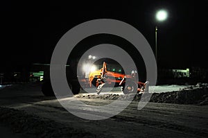 Snow removal tractor cleaning snow, truck silhouette working at night cleaning road, city infrastructure in winter