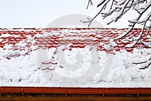 snow rolls down from a metal-tiled roof after a heavy snowfall in winter. Danger of snow falling from roofs