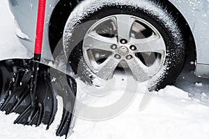 Snow shovel front of car wheel in white snowy day. Winter day routine and problem concept