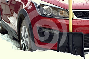 Snow shovel near the bumper of a car stuck in a snowdrift