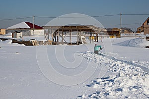 Snow skidded yard in the winter on the farm woman clears the passage to the house in the snow