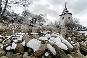 Snow on stones at pebble beach. White church at background