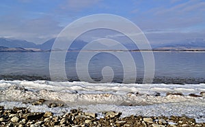 Snow strip at lake shore with mountains in background