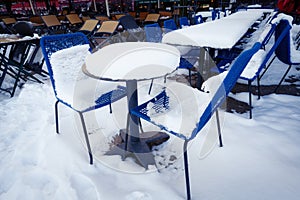 snow on tables and chairs at outdoor gastronomy