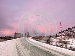 Snow turn on the road stretching away into the distance between the hills. The magical purple color of dawn