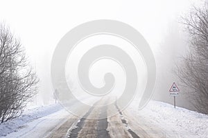 Snow winter landscape. Empty road in fog and Russian slippery road sign