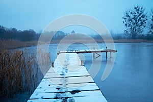 Snow on a wooden pier on the lake shore, view on a foggy December day