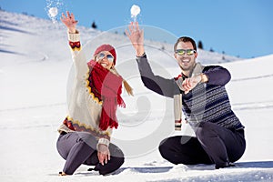 Snowball fight. Winter couple having fun playing in snow outdoors. Young joyful happy multi-racial couple.