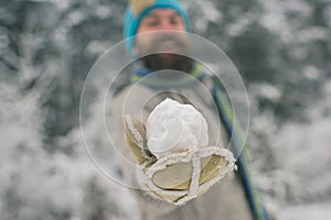 Snowball in hand of blurred bearded man in mittens winter gloves in snowy forest.