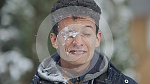 Snowball hitting face of smiling Middle Eastern young man in slow motion. Close-up portrait of surprised guy on snowy