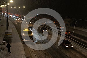 Snowblower and cars on highway in blizzard. Winter in the city. Winter service vehicle at work at night