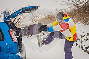 The snowboard does not fit into the car. A snowboarder is trying to stick a snowboard into a car. Humor, fun