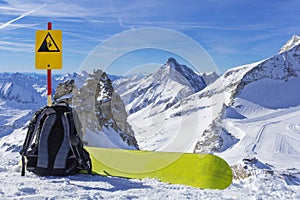 Snowboard equipment, a backpack and a snowboard lie on the edge of a cliff against the background of a panorama of mountains