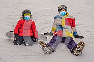 Snowboard instructor teaches a boy to snowboarding wearing a medical mask during COVID-19 coronavirus. Activities for