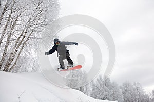 Snowboard jump under the white snowy forest in a good winter day, freeride in a deep snow, ski season