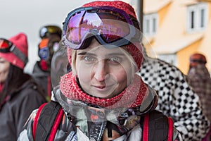 Snowboard pretty blonde girl portrait with green eyes wearing purple mask and orange hat with scarf looking forward.