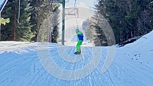 Snowboarder boy go up on t-bar ski lift at alpine resort