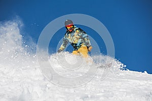 Snowboarder in bright sportswear riding down a powder mountain slope