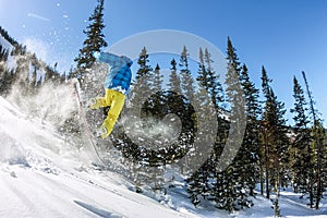 Snowboarder freerider jumping from a snow ramp in the sun on a background of forest and mountains