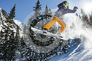 Snowboarder freerider jumping from a snow ramp in the sun on a background of forest and mountains