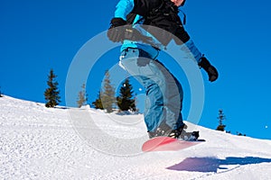 Snowboarder Jumping over Slope on Red Snowboard in the Mountains at Sunny Day. Extreme Snowboarding and Winter Sports