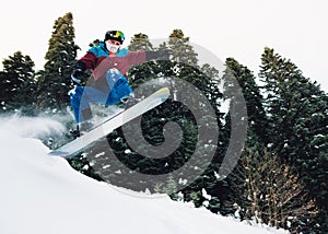 Snowboarder is jumping very high and freeriding from hill in the mountain forest