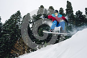 Snowboarder is jumping very high and freeriding from hill in the mountain forest