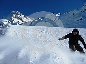 A Snowboarder kicking up powder on a piste