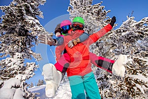 Snowboarder man and woman skier hugging and having fun on background of winter forest and snow. Sunlight in mountains