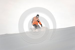 Snowboarder in orange sportswear riding down the mountain slope